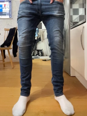 blå replay slim fit  - Snygga blå slim fit jeans med slitningar och tvättade detaljer på benen. Klassisk femficksmodell med knappgylf och smal passform. Jeansen har en modern look och passar perfekt till en avslappnad stil.