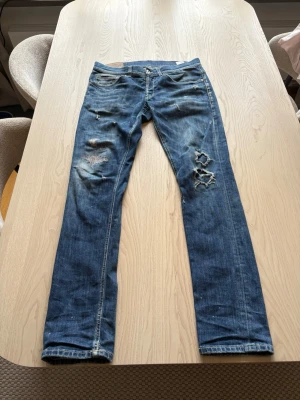 Blå slitna jeans från dondup  - Säljer ett par blå jeans från dondup med slitningar och hål på benen. Jeansen har klassisk femficksmodell och raka ben. Perfekta för dig som gillar en avslappnad och trendig stil.