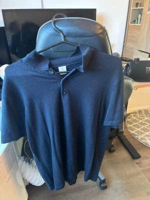 Mörkblå piké från Lindex - Säljer en mörkblå pikétröja från Lindex i storlek 158/164. Skjortan har korta ärmar, klassisk krage och knappar framtill. Perfekt för en avslappnad och stilren look.