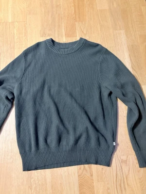 Mörkgrön stickad tröja J.Lindeberg - Snygg mörkgrön stickad tröja från J.Lindeberg i storlek M. Tröjan har rund halsringning, ribbade muddar och är tillverkad i ett mjukt, tätt stickat material. Perfekt för lager på lager och enkel att matcha med jeans eller chinos. Tröjan är använd ett par få gånger 