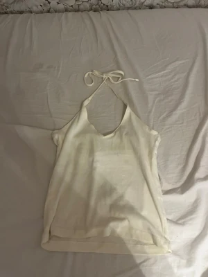 Ljusgul linnetopp med knyt i nacken - Säljer en ljusgul linnetopp med v-ringning och knyt i nacken. Toppen är ärmlös och har en enkel, stilren design som passar perfekt till sommaren. Materialet känns mjukt och lätt mot huden.