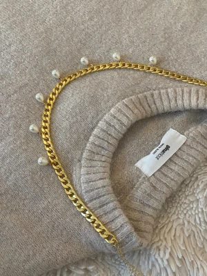 Guldhalsband med pärldetaljer - Snyggt halsband i guldfärgad rostfritt med kedjedesign och vita pärlor som hänger längs hela halsbandet. Perfekt accessoar för att lyfta din outfit med en trendig och elegant touch. Passar till många olika stilar och är lätt att matcha.