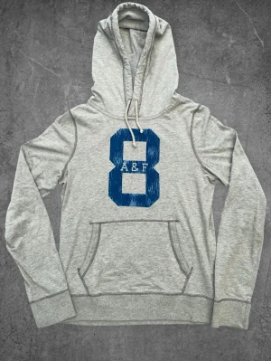 Vintage Abercrombie And Fitch hoodie - Grå - Vintage Abercrombie And Fitch hoodie - Grå   Storlek: M Skick: Mycket bra Defekt: Liten fläck på vänster sida nere, se sista bilden. Hör gärna av dig om du har några frågor, vill ha mått eller fler bilder!