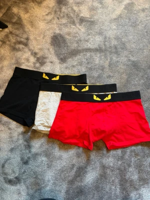 3-pack fendi kalsonger (aldrig använda!) - Säljer ett 3-pack kalsonger i svart, grått och rött. Alla har bred svart resår med ett gult ögonmotiv framtill. Modellen är boxershorts och materialet känns mjukt och stretchigt, perfekt för vardagskomfort.