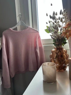 Ljusrosa stickad tröja - Mysig ljusrosa stickad tröja med rund halsringning och långa ärmar. Tröjan har en avslappnad passform och är tillverkad i ett mjukt, fluffigt material som känns skönt mot huden. Perfekt för kyligare dagar och enkel att matcha med olika outfits. Köpt på lager 157. Storlek S💕