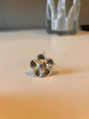 Silverfärgad blomring i metall - Ringen sägs vara vattentät men det är en liten rost fläck på ett av bladen inne vid diamanten, den är jätte fin och snygg men jag har lite för många ringar just nu så jag bara valde någon. Mitt ring finger är 6 vem i omkrets och den sitter perfekt (ringen går att justera storlek på).