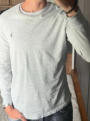 Polo Ralph Lauren långärmad t-shirt i ljusgrå - stl M - Polo Ralph Lauren långärmad t-shirt i ljusgrå, storlek M. 100% bomull, tunn och mjuk, sitter nära kroppen. Personen på bilden är 189cm, väger 78kg.  Använd men i mycket fint skick, inga hål eller fläckar.  Rök- och djurfritt hem. Skriv gärna om du vill ha fler bilder eller undrar något!