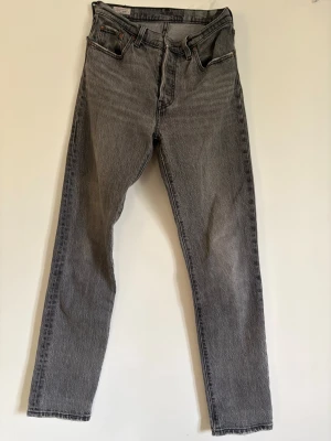 Lives 501 Grå raka jeans med vintagekänsla använt få gånger  - Säljer ett par grå jeans med rak passform och klassisk femficksdesign. Jeansen har en hög midja och subtilt slitna detaljer för en cool vintage-look. Tillverkade i kraftigt denimtyg som ger en tidlös och avslappnad stil. 