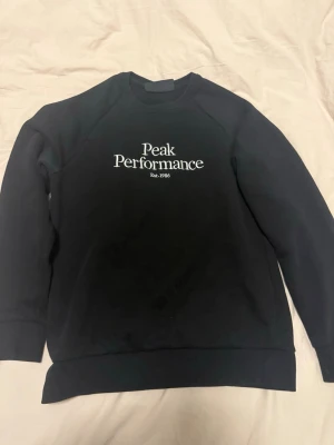 Svart sweatshirt Peak Performance M - Säljer en svart sweatshirt från Peak Performance i storlek M. Tröjan har rund halsringning och vit logga broderad på bröstet. Tillverkad i mjukt material med ribbade muddar vid ärmslut och nederkant. Perfekt för en clean och stilren look.