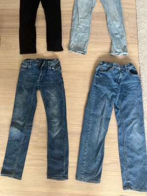 Fyra par jeans i olika tvättar - Fyra par jeans i olika färger och passformer. Ett par svarta, ett par ljusblå, samt två par blå jeans med olika tvättar och slitningar. Klassisk femficksmodell och raka eller smala ben. 