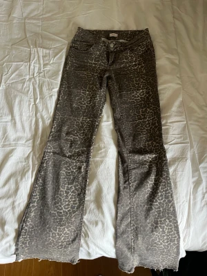 Bruna leopardmönstrade bootcut jeans - Säljer ett par bruna jeans med leopardmönster och bootcut-modell. Jeansen har råa kanter nertill, fem fickor och dubbla knappar i midjan. Materialet är denim med stretch för extra komfort. Perfekta för dig som vill sticka ut med ett djuriskt mönster!Titta sista bilden för att se defekten på fickad baktill! 