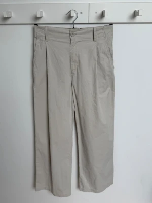 Beige chinos med raka ben - Snygga beige chinos med raka ben och hög midja. Byxorna har sidofickor fram och två bakfickor med knapp. Tillverkade i ett lätt och mjukt bomullstyg som ger en clean och avslappnad look. Perfekta för en stilren och enkel outfit. Använda något tillfälle, nyskick. Nypris 600.