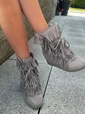 Grå boots med fransar och kilklack - Säljer ett par grå boots med kilklack och massor av fransar längs skaftet och framtill. Skorna har snörning och är gjorda i mockaliknande material. Perfekta för dig som vill sticka ut med en unik och trendig stil. I gott skick används 3 gånger ungefär.
