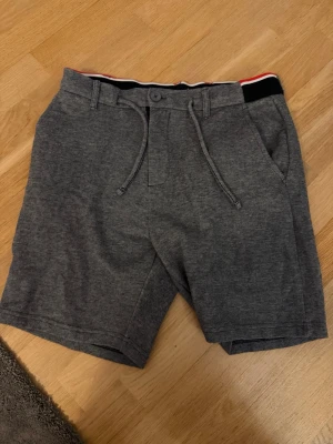 Grå shorts med snörning från SMOG - Snygga grå shorts från SMOG med snörning i midjan och praktiska sidofickor. Tillverkade i mjukt bomullsmaterial för skön känsla. Perfekta för varma dagar och enkel att matcha med olika stilar.