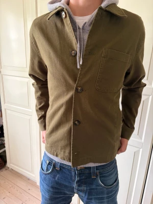 Olivgrön only & sons overshirt med bröstficka - Stilren olivgrön overshirt i kraftigt bomullstyg med klassisk krage och tre knappar framtill. Har en enkel bröstficka på vänster sida och raka ärmar. Perfekt att bära över en hoodie för en avslappnad look. Overshirten är i storlek Moch är helt ny. Hör av er vid frågor och priset är inte hugget i sten!