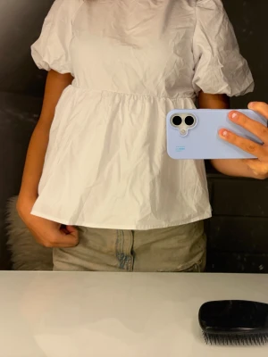 Vit blus med puffärm och öppen rygg - Supersöt vit blus med puffärmar och en luftig passform. Baksidan har öppen rygg med knytband upptill och en stor rosett i midjan. Perfekt till jeans eller kjol för en trendig look.