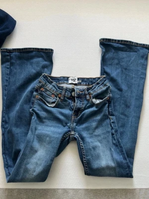 Blå bootcut jeans från 157 - Snygga blå bootcut jeans från 157 med klassisk femficksdesign och ljus tvätt. Jeansen har normal midja, dragkedjegylf och bruna sömmar. Perfekta för dig som gillar en avslappnad men trendig look.