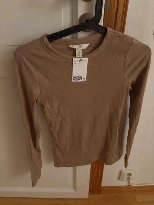 Beige långärmad topp  - Säljer en enkel beige långärmad topp från H&M. Toppen är ribbad och har en rund halsringning. Perfekt att matcha med jeans eller kjol för en clean look. 