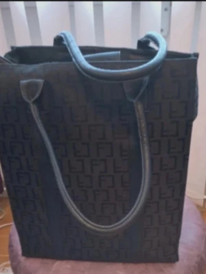 Svart shoppingväska Friis Company - Stilren svart shoppingväska från Friis Company med präglat mönster och handtag i skinn. Väskan har dragkedja och knäppning upptill, två små innerfack, ett större fack med dragkedja samt ett löstagbart myntetui i skinn. Perfekt för dig som vill ha både stil och funktion.