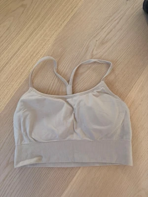 Beige seamless bh med smala band - Säljer en beige seamless bh med smala axelband och brottarrygg. Bh:n har bred resår under bysten och är tillverkad i ett mjukt, stretchigt material. Perfekt för dig som vill ha en enkel och bekväm bh utan byglar.
