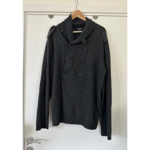 JOOP! Mörkgrå stickad tröja, 100% ull - storlek XL - Mörkgrå stickad tröja från JOOP! i storlek XL. Stilren modell med en dubbelknäppt design framtill och bred krage och axelklaffar med knappar. Ärmarna är långa och har förstärkta armbågspartier i samma färg och material. Supermjukt material i 100% ull. Kvalitetströja som kommer hålla säsong efter säsong. Nypris 1800:-. Mycket gott skick, som ny.