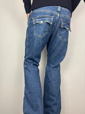 Levi’s Noughties Bootcut Jeans Blå W34 – Vintage 00-tal - Levi’s "Noughties Bootcut" jeans med unika lockfickor och tidlös 00-talslook. Färg: Blå mellantvätt Passform: Bootcut Storlek: W34  Skick: Mycket bra begagnat skick (A/B Grade). Mått [platt] (±1 cm): A: 47 cm B: 95 cm D: 31 cm C: 26 cm För korta på mig i bilden som är 189 cm, har fått dra ner jeansen rejält i syfte att visa passform.  Tveka inte att höra av dig vid frågor eller funderingar.  Skickas snabbt!