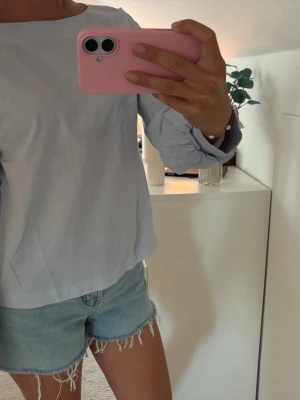 Ljusblå blus med långa ärmar - Snygg ljusblå blus i rak modell med långa ärmar och resår vid ärmsluten. Tillverkad i ett tunt, vävt material som ger en fräsch och stilren look. Perfekt att matcha med jeans eller kjol för en enkel men trendig outfit.