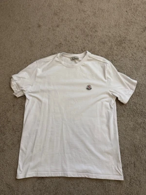 Vit t-shirt från Moncler - Klassisk vit t-shirt från Moncler med rund hals och diskret Moncler-logga broderad på bröstet. Tillverkad i mjuk bomull och har en enkel, clean look som passar till allt.