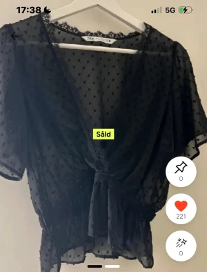 slutsåld zara blus - Snygg svart transparent blus från Zara med prickigt mönster och spetsdetaljer vid halsen. Blusen har korta ärmar och knyt i midjan som ger en feminin siluett. Perfekt att styla med ett linne under för en trendig look.
