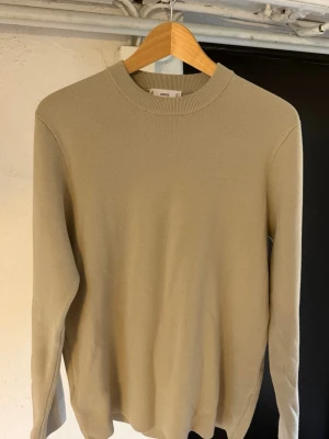 Beige stickad tröja från Mango - En stilren beige stickad tröja från Mango med rund halsringning och långa ärmar. Tröjan har en enkel och klassisk design som passar perfekt till många olika outfits. Materialet är mjukt och bekvämt.