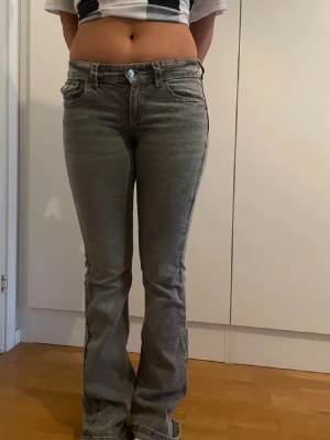 Grå bootcut jeans med låg midja - Säljer ett par gråa bootcut jeans med låg midja och klassisk femficksdesign. Jeansen har en lätt tvättad look och är tillverkade i ett stretchigt denimtyg som sitter snyggt på benen. Perfekta för en avslappnad och trendig stil.
