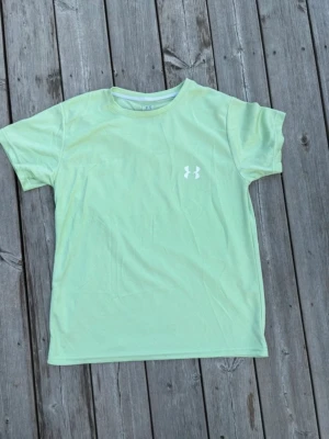 Ljusgrön t-shirt från Under Armour - Storlek S. Snygg ljusgrön t-shirt från Under Armour med klassisk logga på bröstet. T-shirten har rund halsringning och korta ärmar. Perfekt för träning eller chill dagar. Tillverkad i ett mjukt och lätt material som andas. Hör av er vid intresse