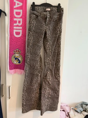 Leopardmönstrade bootcut jeans Nelly - Säljer ett par snygga leopardmönstrade jeans från Nelly. Modellen har bootcut-ben och hög midja. Jeansen är i grå och beige toner med två knappar framtill och bälteshällor. Perfekta för dig som vill sticka ut med ett djurmönster!
