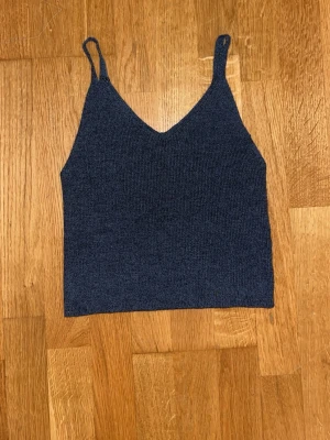 Mörkblå stickad linnetopp - Mörkblå stickad linnetopp med smala axelband och v-ringad hals. Toppen är croppad och har en enkel, stilren design som passar perfekt till jeans eller kjol. Materialet känns mjukt och bekvämt mot huden.