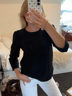 Svart blus med puffärm - Stilren svart blus med rund halsringning och diskreta puffärmar. Blusen har en rak passform och är tillverkad i ett lätt tyg som ger en snygg siluett. Perfekt att matcha med både jeans och kjol för en trendig look.