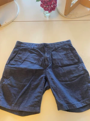 Mörkblå bomullsshorts med fickor - Snygga mörkblå shorts i bomull med normal passform. Shortsen har två sidofickor fram och två bakfickor med knapp, samt bälteshällor och stängs med knapp och dragkedja. Perfekta för varma dagar och enkel att matcha med olika stilar.