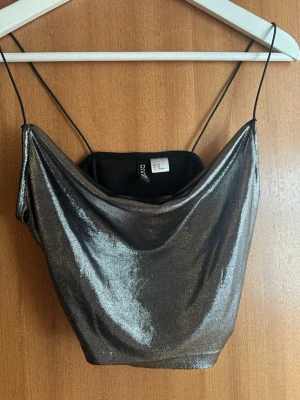 Glittrig silver linnetopp från H&M - Snygg glittrig silverfärgad linnetopp från H&M Divided med tunna axelband och draperad urringning. Perfekt för dig som vill sticka ut och addera lite extra shine till din outfit. Materialet är mjukt och följsamt syntet.