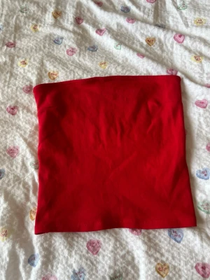 Röd bandeau tubtopp från Gina Tricot - Säljer en röd bandeau tubtopp från Gina Tricot i ribbad bomullsmix. Toppen är ärmlös och har en enkel, clean look som passar perfekt till sommaren. Superenkel att styla med både jeans och kjol!