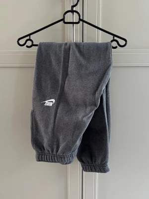 Mörkgråa mjukisbyxor från Nike - Snygga mörkgråa mjukisbyxor från Nike med klassisk vit logga på benet. Byxorna har resår i midjan och vid bensluten samt två sidofickor. Se separat annons för matchande överdel.
