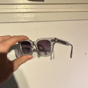 Chimi transparenta solglasögon - Snygga solglasögon från Chimi med transparent båge och fyrkantig form. Glasen är mörktonade i grått och ger en cool vibe. Kommer med originaletui och tygpåse. Perfekta för dig som vill sticka ut med stilrena accessoarer.