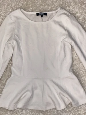Vit topp med volang (passar även som xs-s) - Strl M men passar även som XS- S!! Toppen har en markerad midja och volang nedtill som ger en feminin siluett + korta ärmar. Den har också ett mjukt och stretchigt material som sitter bekvämt💞