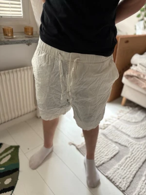 Vita linneshorts  - Säljer ett par vita shorts i linne med avslappnad passform och dragsko i midjan. Shortsen har resår i midjan och en bakficka. Perfekta för sommaren och riktigt sköna att bära till vardags.