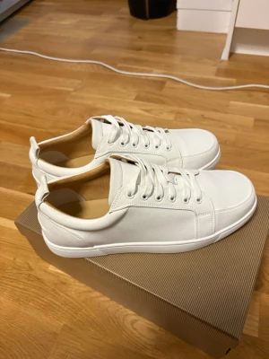 Vita låga sneakers med röd sula - Stilrena vita sneakers med lågt skaft och klassisk snörning. Skorna har en unik röd sula med präglad text och är tillverkade i slätt läder. Perfekta för dig som gillar minimalistisk och clean stil. Skorna har materialet läder och väldigt sköna 