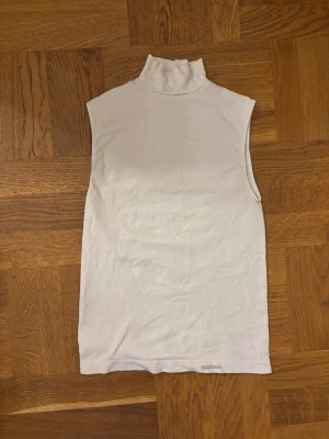 Vit ärmlös polotopp - Säljer en stilren vit polotopp utan ärmar. Toppen har en hög krage och är figurnära i modellen, vilket ger en clean och modern look. Perfekt att matcha med jeans eller kjol för en enkel men snygg outfit.