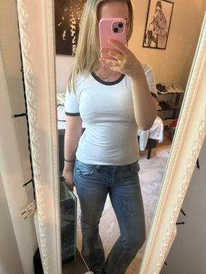 Vit tight t-shirt med svarta detaljer - Säljer en vit t-shirt med svarta kanter vid halsringning och ärmslut. T-shirten har en tight passform och korta ärmar. Perfekt till jeans eller kjol för en enkel och stilren look.