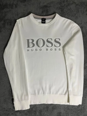BOSS Hugo Boss – White Reflective Logo Sweatshirt (L fit M)  - Elegant and high-quality Hugo Boss sweatshirt in crisp white, featuring a stunning reflective BOSS logo on the front. Size L, fits well also for M size. Length 65 cm, pit-to-pit 56 cm – comfortable and modern fit.  ✅ Condition: Excellent – no wear, no stains 💯 Authenticity: 100% genuine Hugo Boss garment 📦 Shipping: Dispatched immediately after purchase – fast and reliable delivery!  This sweatshirt blends Hugo Boss’s minimalist design with premium craftsmanship. The reflective logo