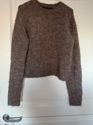 Brun fluffig stickad tröja Vero Moda - Mysig brun stickad tröja från Vero Moda i storlek S. Tröjan har en fluffig och mjuk textur, rund halsringning och långa ärmar. Perfekt för kyliga dagar och enkel att matcha med jeans eller kjol.