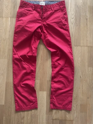 Röda chinos från Esprit  - Snygga rosa chinos med rak passform och klassisk design. Byxorna har fickor fram och bak samt bälteshällor i midjan. Perfekta för dig som vill sticka ut med färg och ändå hålla det stilrent. Materialet är mjukt och bekvämt, troligtvis bomull.