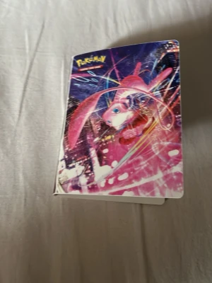 Pokémon samlarkortalbum - Säljer två Pokémon samlarkortalbum med färgglada omslag, ett med Mew i rosa och lila toner och ett med Mewtwo i blått och grönt. Perfekt för att organisera och visa upp dina Pokémonkort. Albumen har officiell Pokémon-design och plats för många kort.