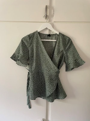 Grön topp - Grön omlott topp med prickar, knytes med bandet. Storlek S, fint skick. 